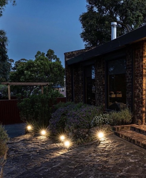 Garden and path lighting switched on outside a brick home at dusk