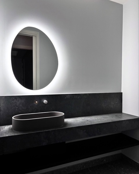 A backlit round mirror above a stone vanity