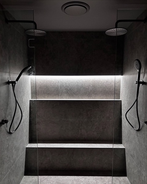 A tiled shower with a lit recessed niche