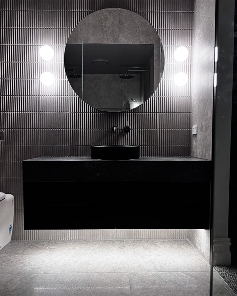 A bathroom with a round mirror and wall lights either side