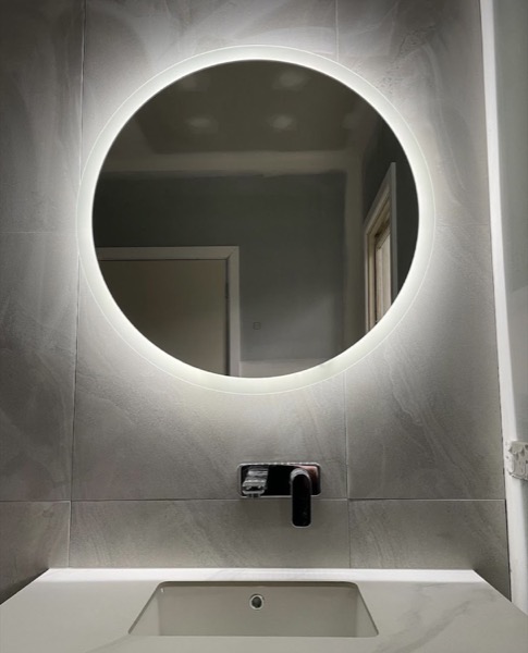A bathroom with a backlit round mirror above the bath