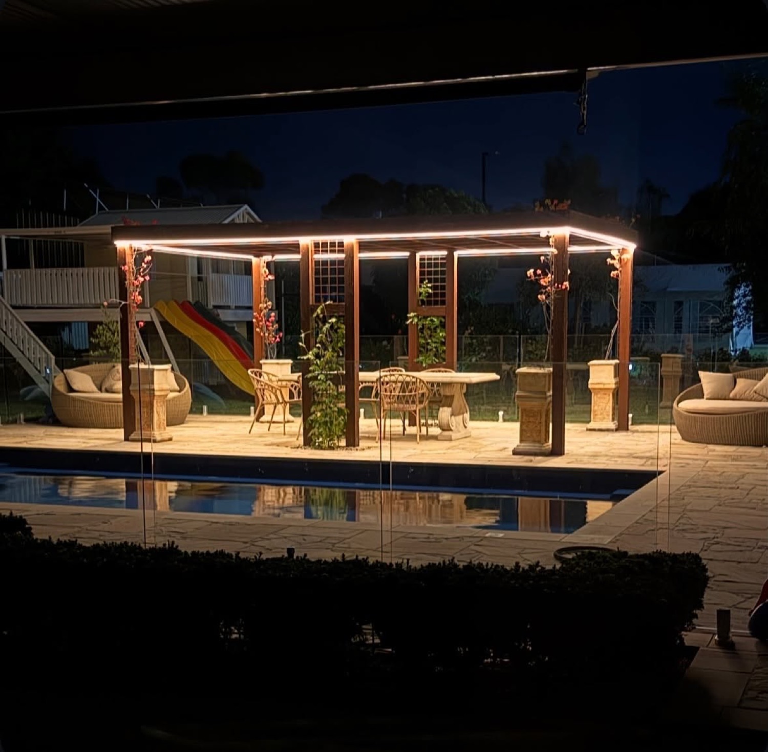A pergola over a swimming pool lit with warm strip lighting at night