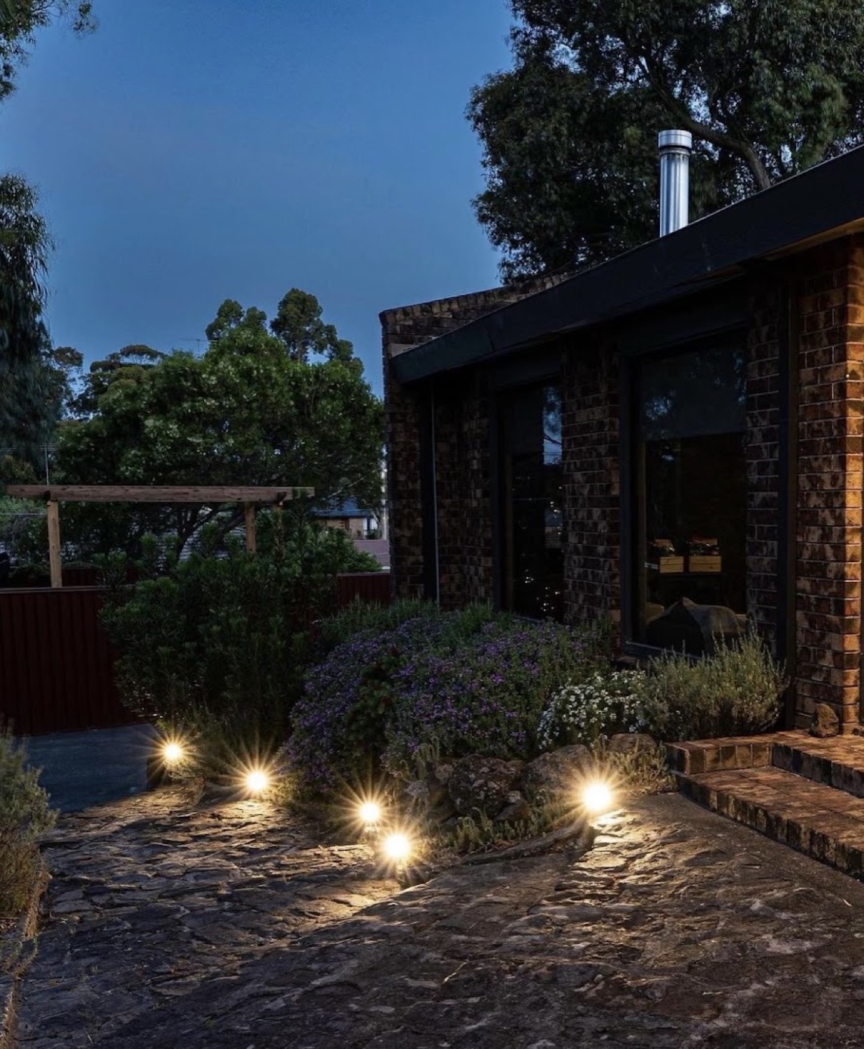 Garden and path lighting switched on outside a home at dusk