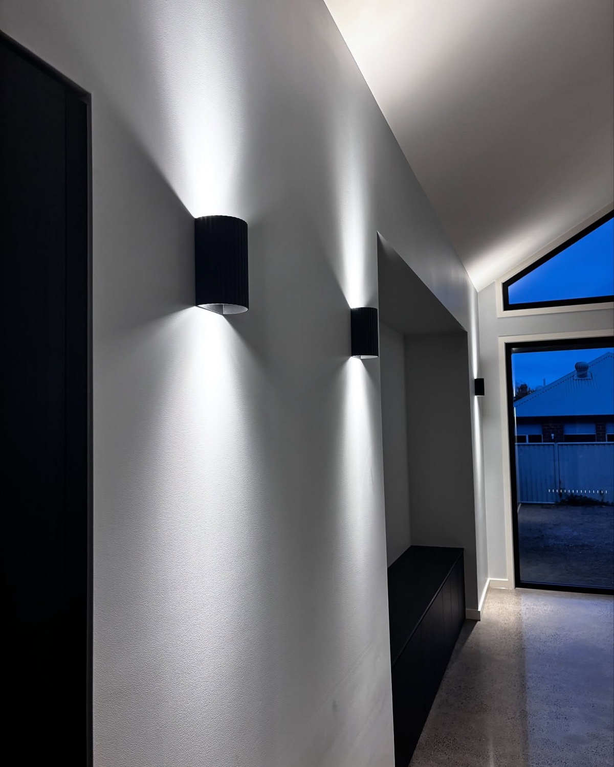 A hallway lit by black up and down wall lights