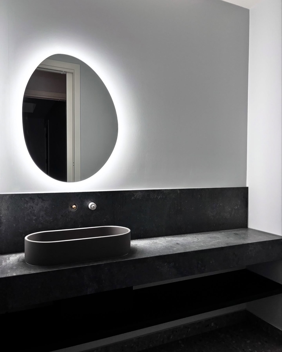 A backlit round mirror above a stone vanity