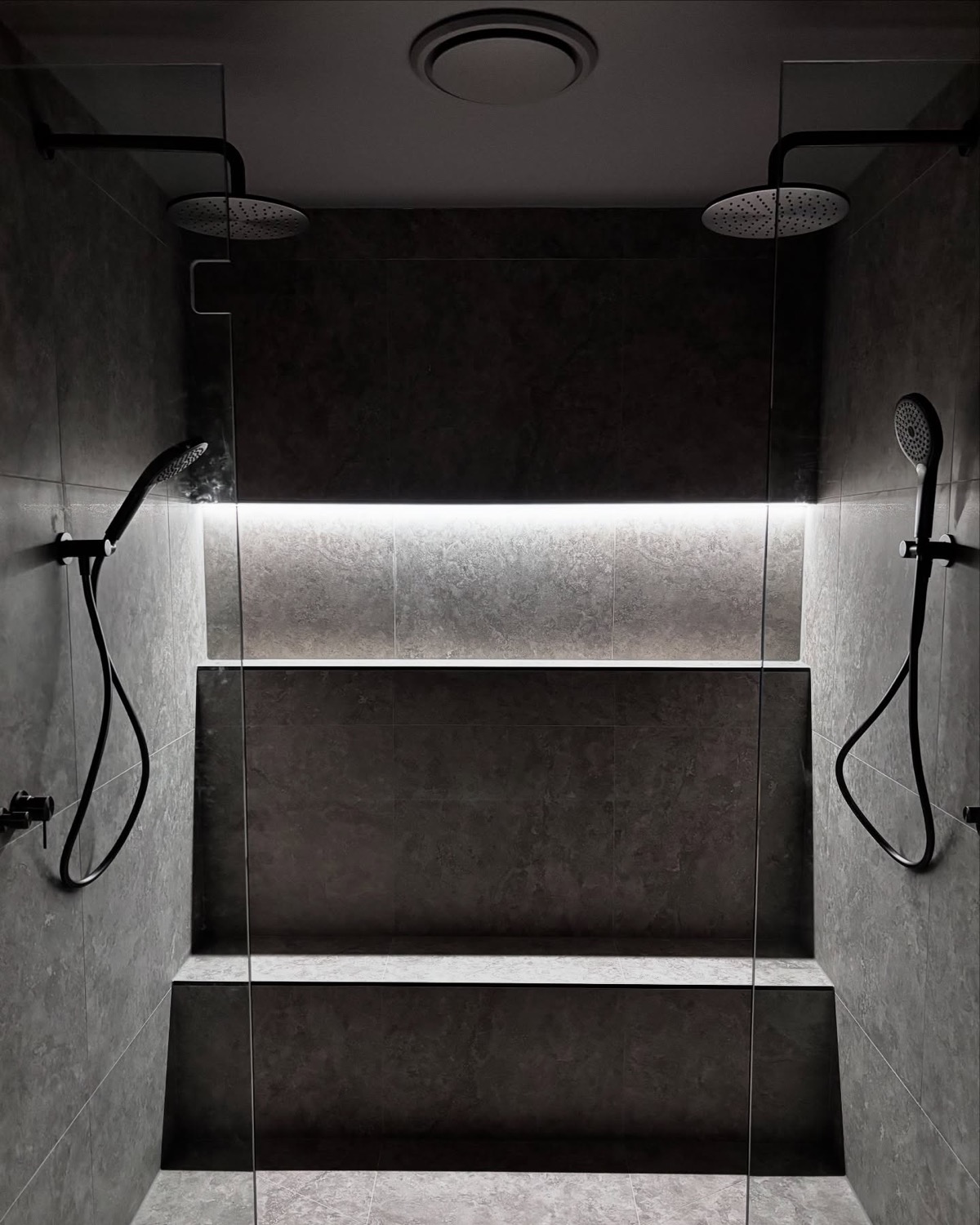 A tiled shower with a lit recessed niche