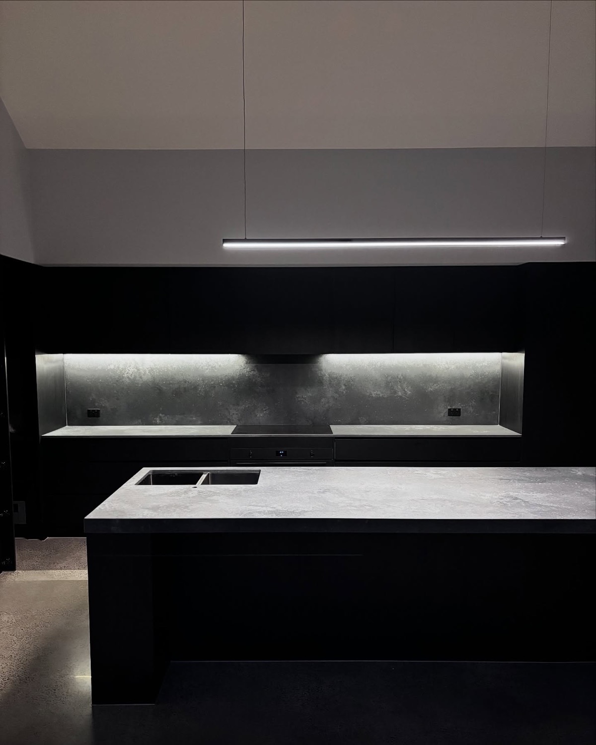 A dark kitchen island with a lit splashback recess